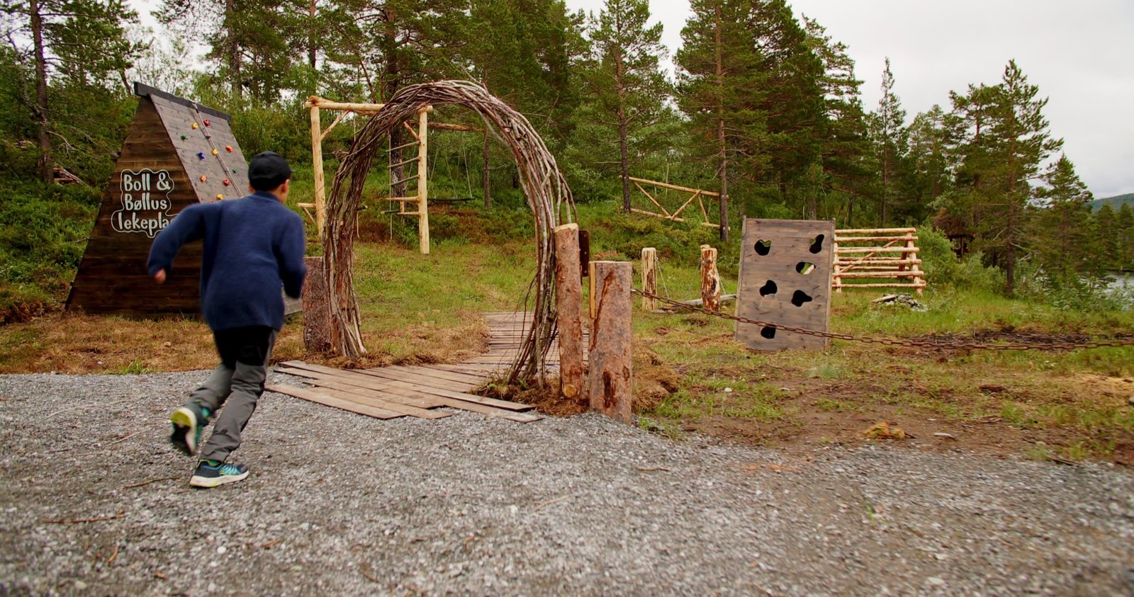 Barn løper over naturlekeplassen ved lavvoen, med klatrestativ av tre